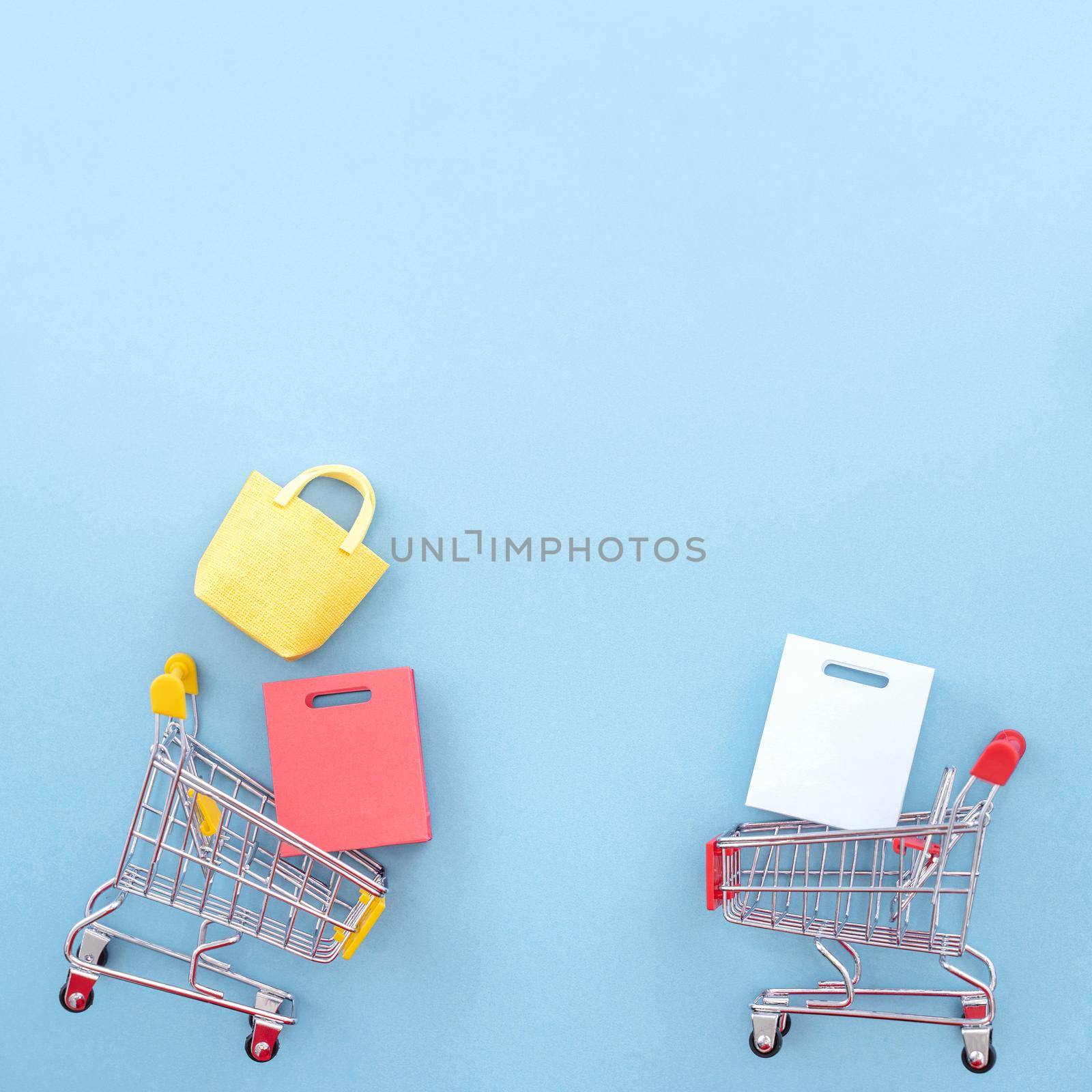 Abstract design element, concept of annual sale, shopping season - mini yellow cart with paper bag isolated on pastel blue background, top view, flat lay.