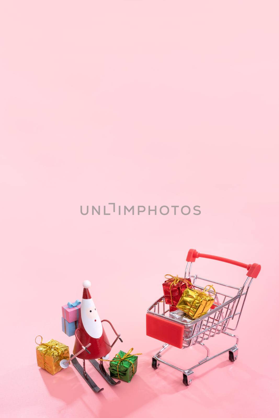 Christmas shopping concept, mini red shop cart trolley with Santa Claus toy and gift box isolated on pale pink background, blank copy space, close up by ROMIXIMAGE