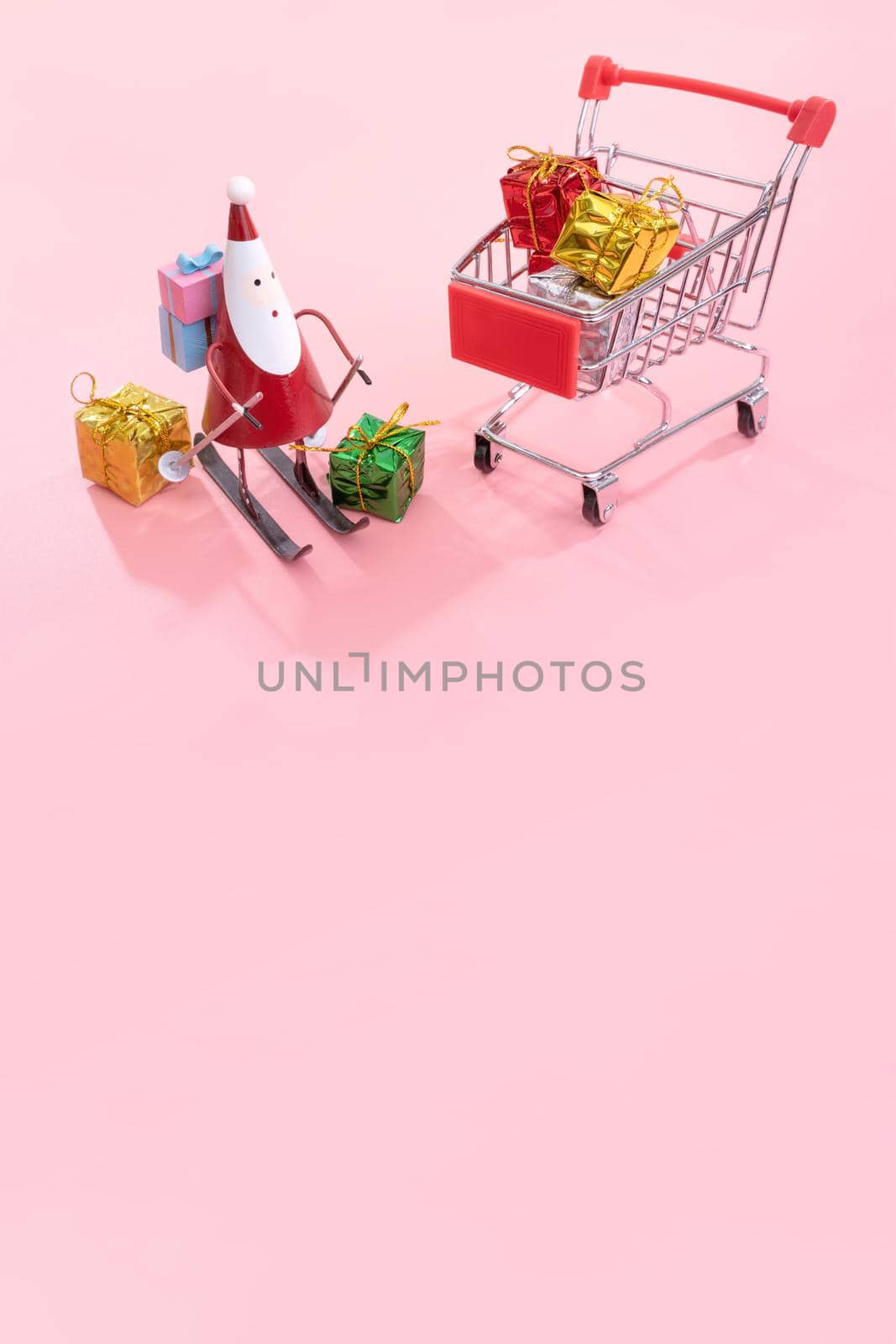 Christmas shopping concept, mini red shop cart trolley with Santa Claus toy and gift box isolated on pale pink background, blank copy space, close up by ROMIXIMAGE