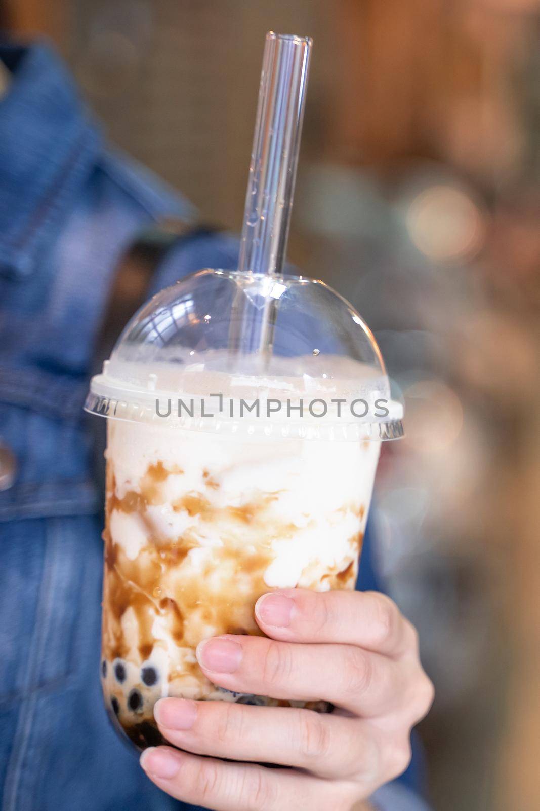 Young woman is holding, drinking brown sugar flavored tapioca pearl bubble milk tea with glass straw in night market of Taiwan, close up, bokeh by ROMIXIMAGE