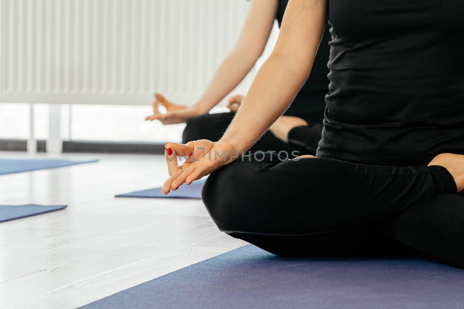 Close up of yoga women sitting in lotus asana during yoga class, cropped view by Mariakray