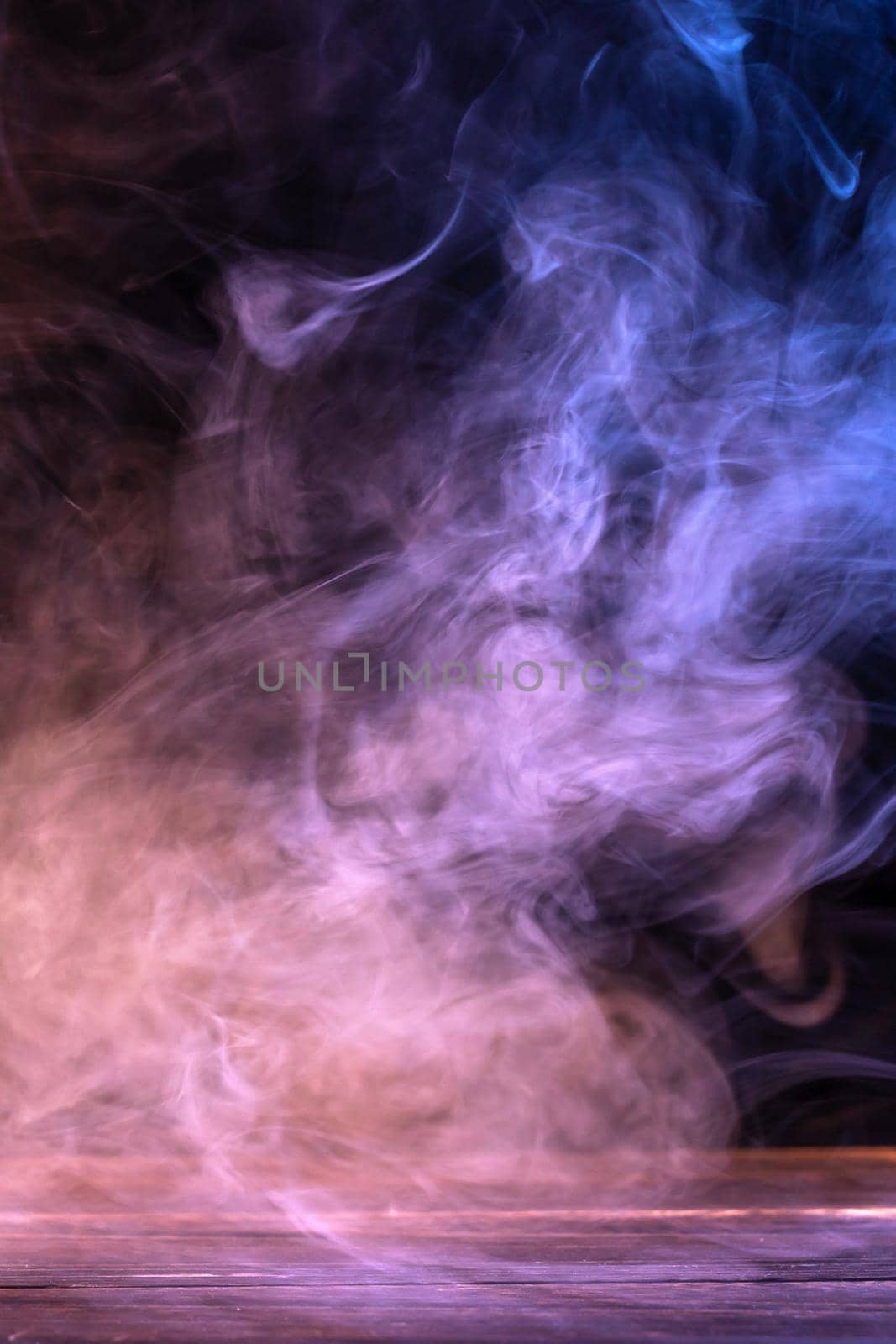 Conceptual image of multi-colored smoke isolated on dark black background and wooden table. by ROMIXIMAGE
