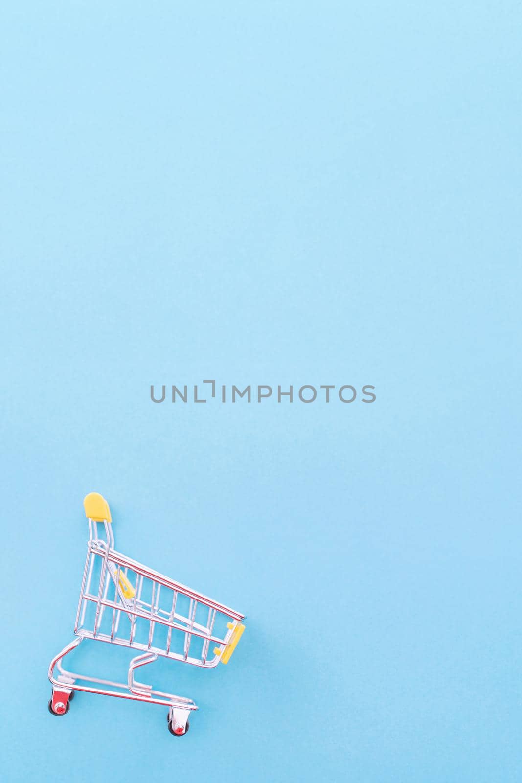 Abstract design element, annual sale, shopping season concept, mini yellow cart with colorful paper bag on pastel blue background, top view, flat lay