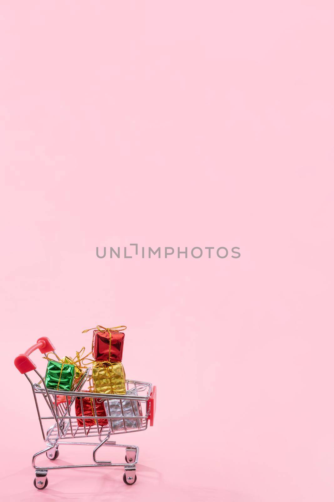Annual sale, Christmas shopping season concept - mini red shop cart trolley full of gift box isolated on pale pink background, copy space, close up