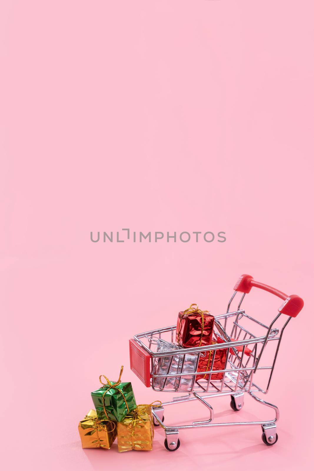 Annual sale, Christmas shopping season concept - mini red shop cart trolley full of gift box isolated on pale pink background, copy space, close up by ROMIXIMAGE