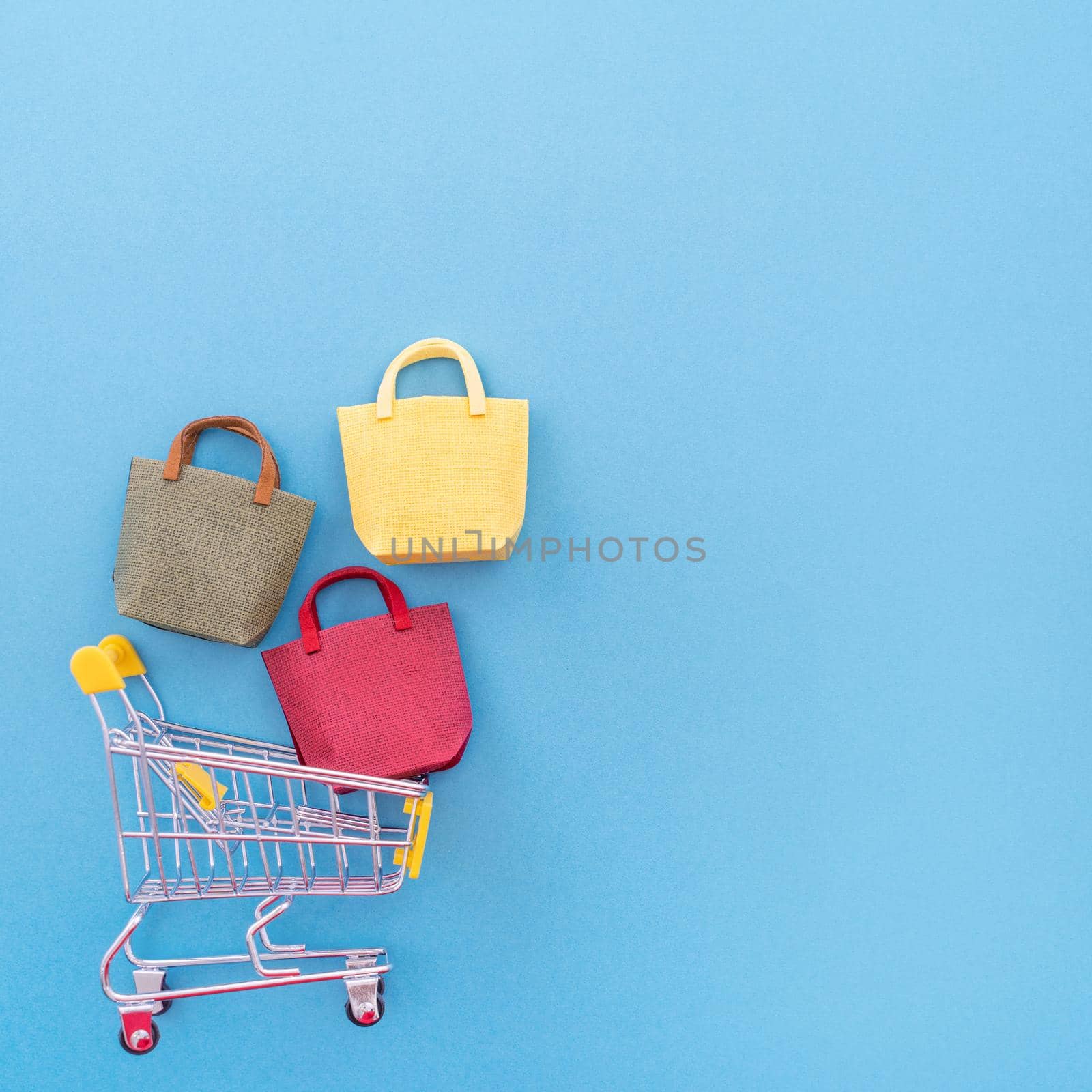 Abstract design element, concept of annual sale, shopping season - mini yellow cart with paper bag isolated on pastel blue background, top view, flat lay. by ROMIXIMAGE