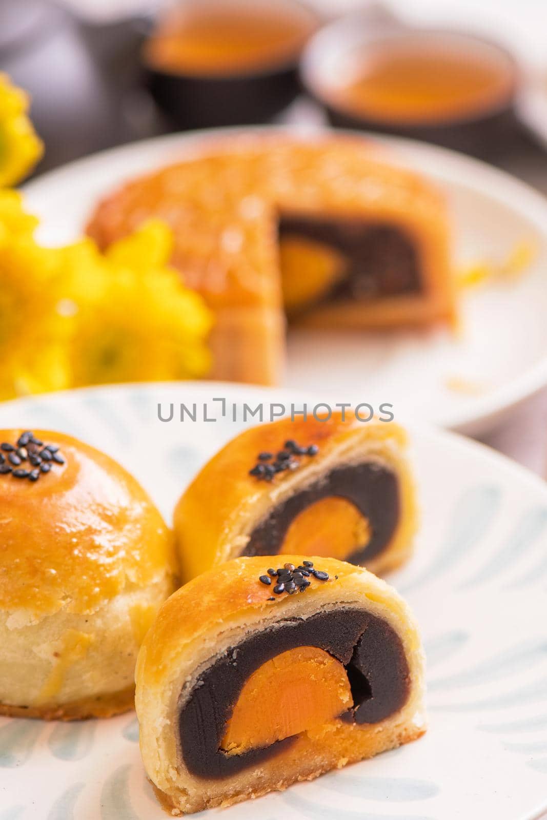 Mid-Autumn Festival traditional food concept - Beautiful cut moon cake on blue pattern plate on white background with flower, close up, copy space
