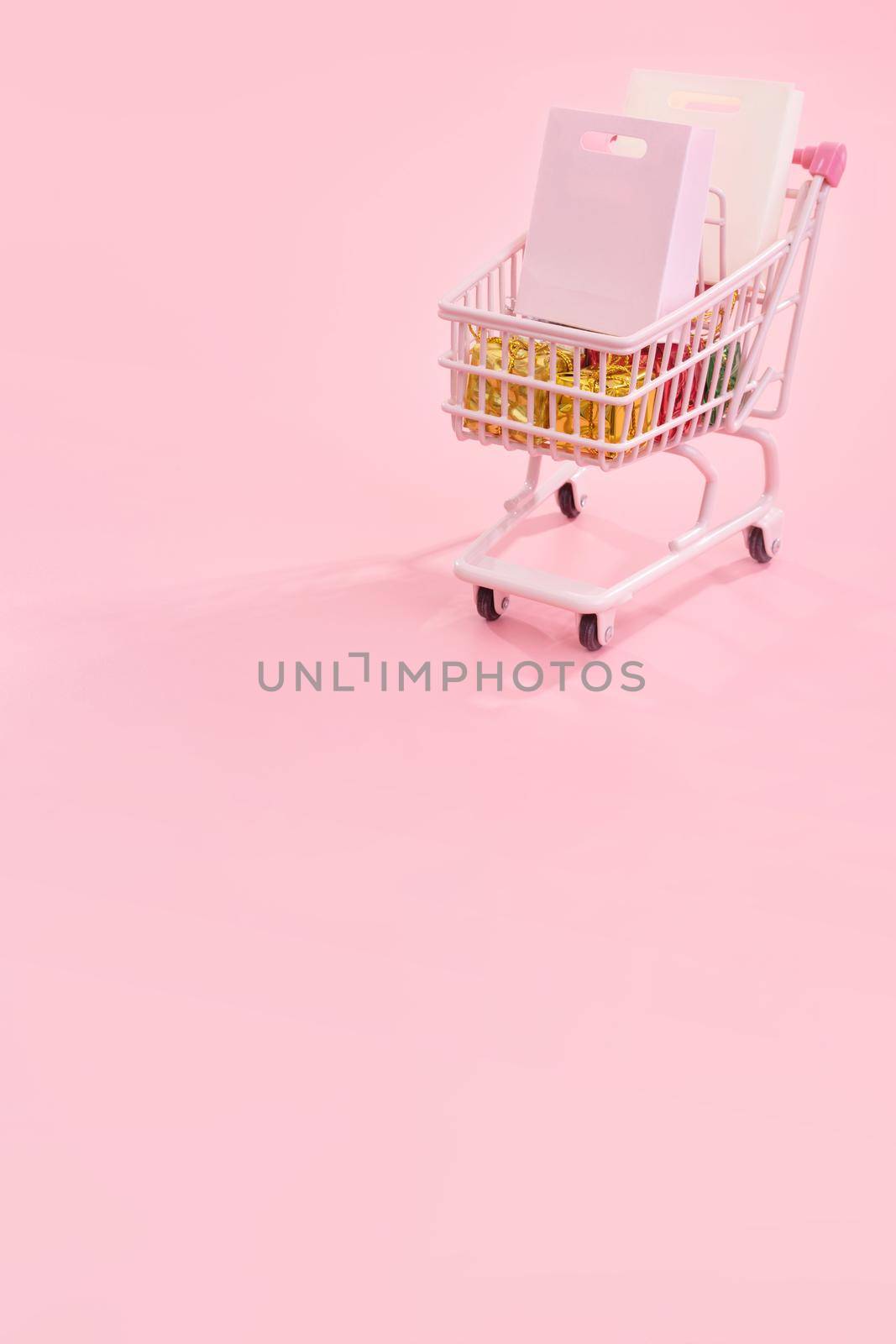 Annual sale shopping season concept - mini red shop cart trolley full of paper bag gift isolated on pale pink background, blank copy space, close up by ROMIXIMAGE