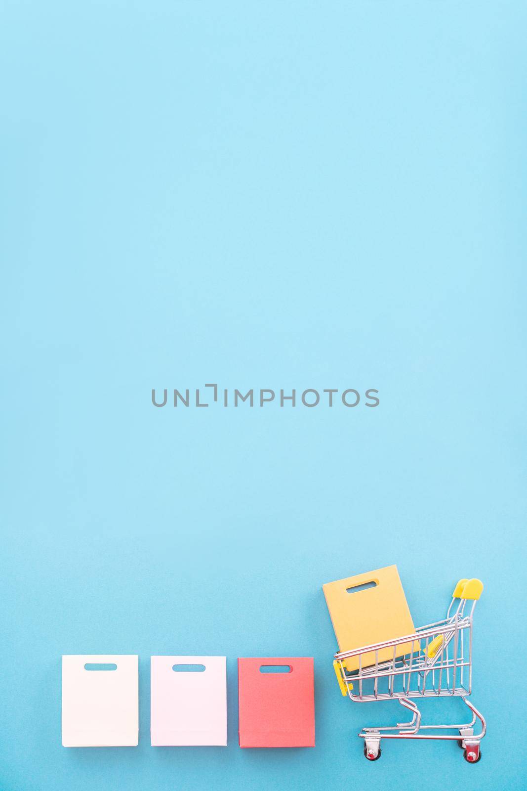 Abstract design element, concept of annual sale, shopping season - mini yellow cart with paper bag isolated on pastel blue background, top view, flat lay.