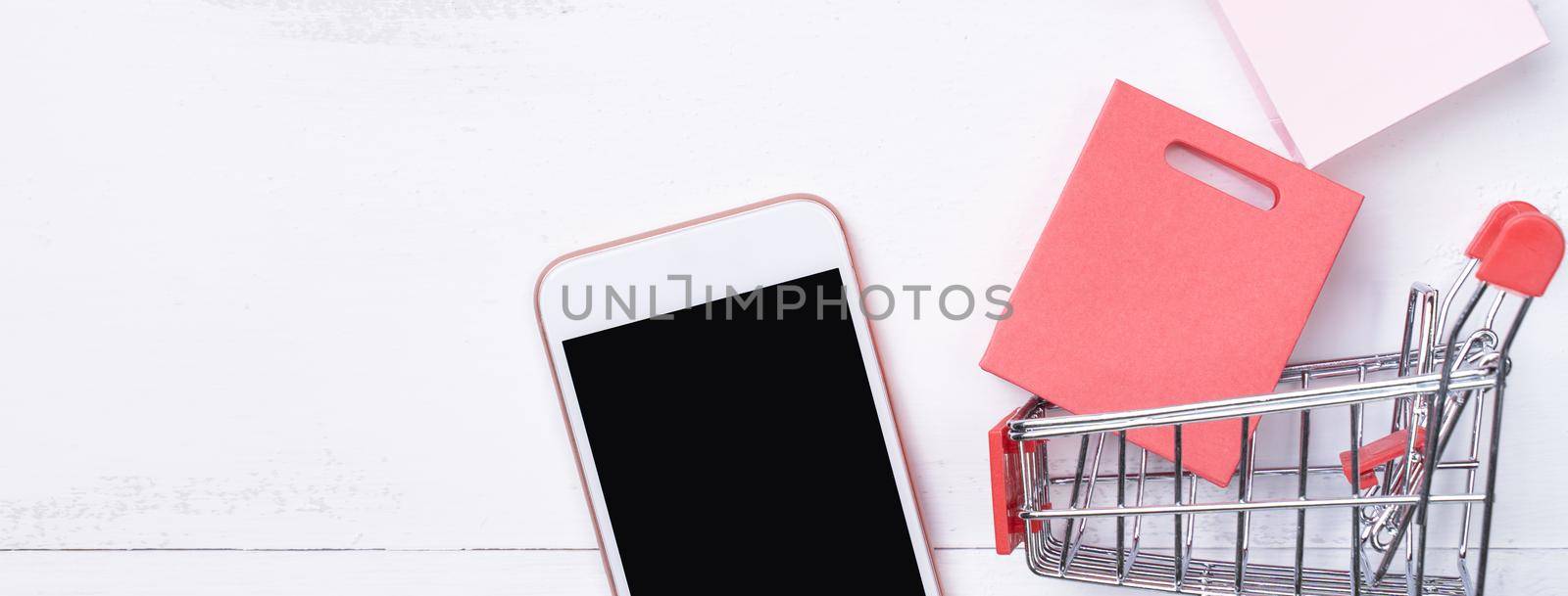 Abstract online shopping, mobile payment concept design element, colorful cart and paper bags on white wooden table background, top view, flat lay