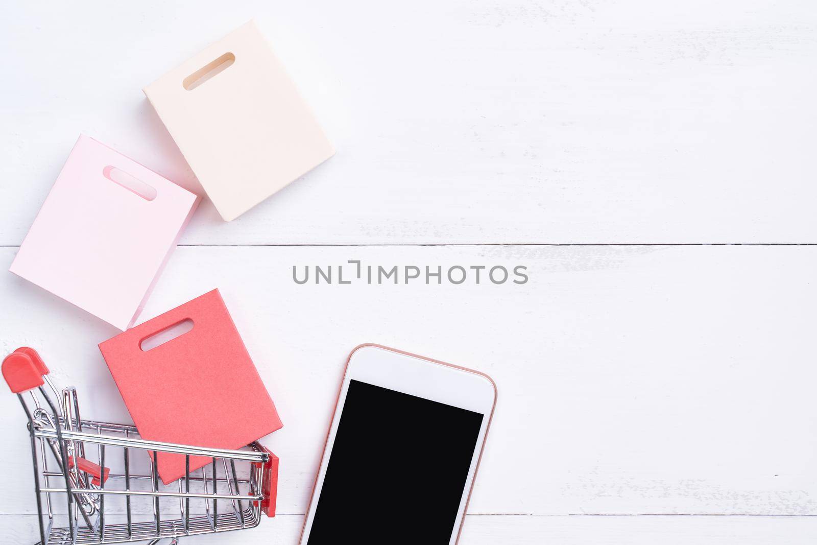 Abstract online shopping, mobile payment concept design element, colorful cart and paper bags on white wooden table background, top view, flat lay