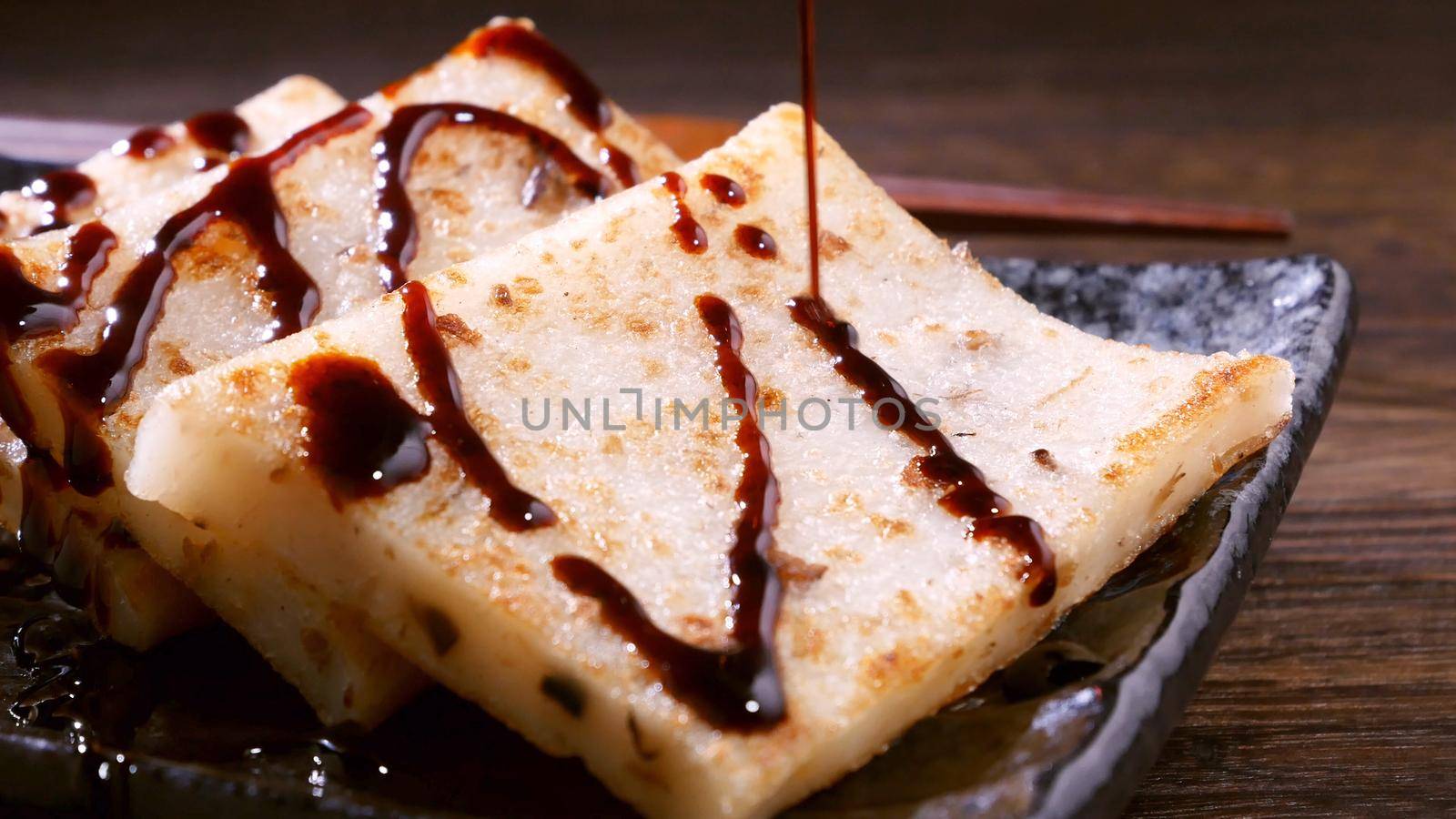 Pouring black soy sauce on ready-to-eat delicious turnip cake, Chinese traditional local dish radish cake in restaurant, close up, copy space.