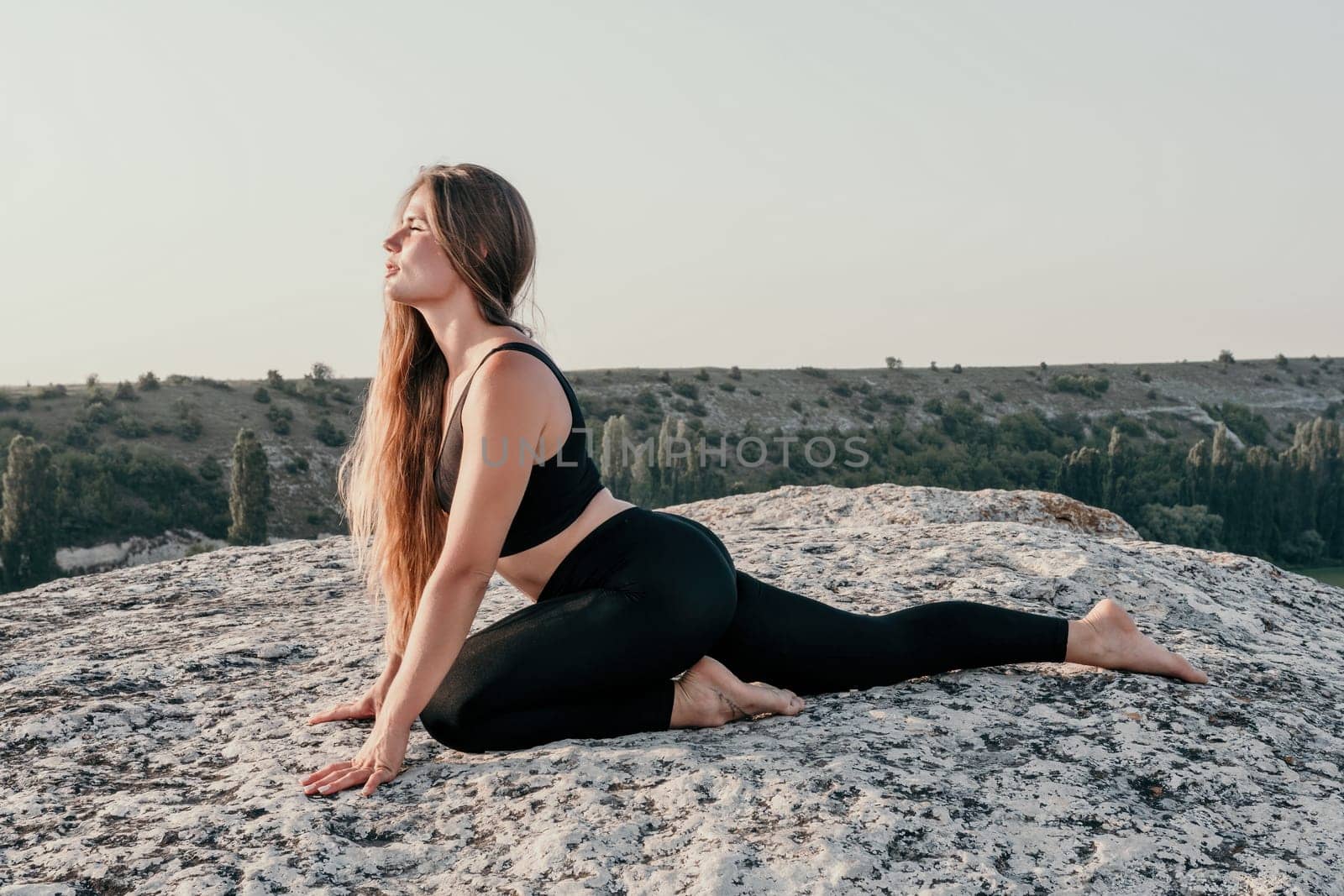 Fitness woman. Well looking middle aged woman with long hair, fitness instructor in leggings and tops doing stretching and pilates on the rock near forest. Female fitness yoga routine concept. by panophotograph