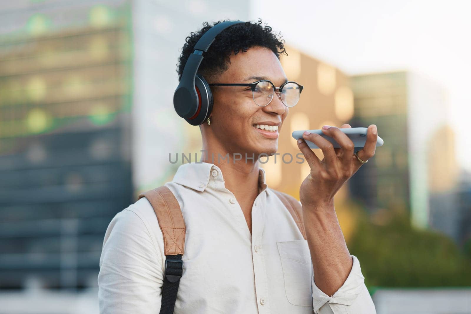 Man, 5g phone and voice note in the city traveling to university lesson and using his mobile. College student, travel and cellphone call using headphones in an urban town on the way to school by YuriArcurs