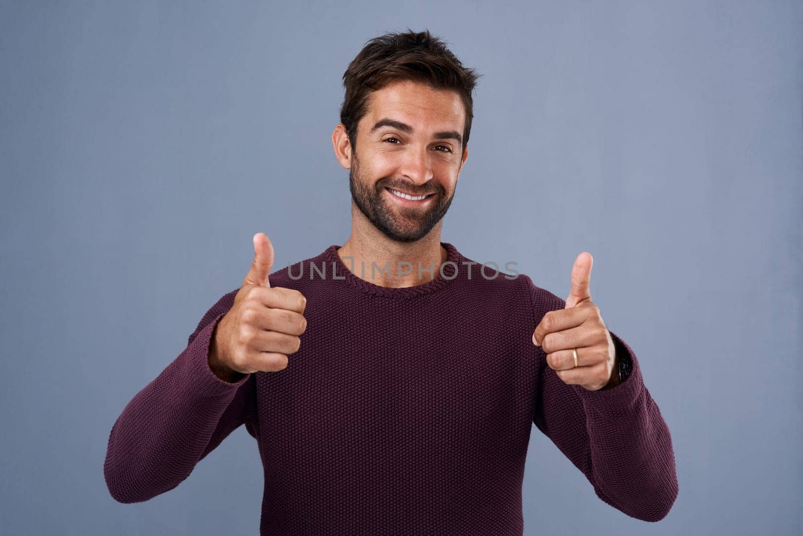 Hey Good on you. Studio shot of a handsome young man giving a thumbs up gesture against a gray background. by YuriArcurs