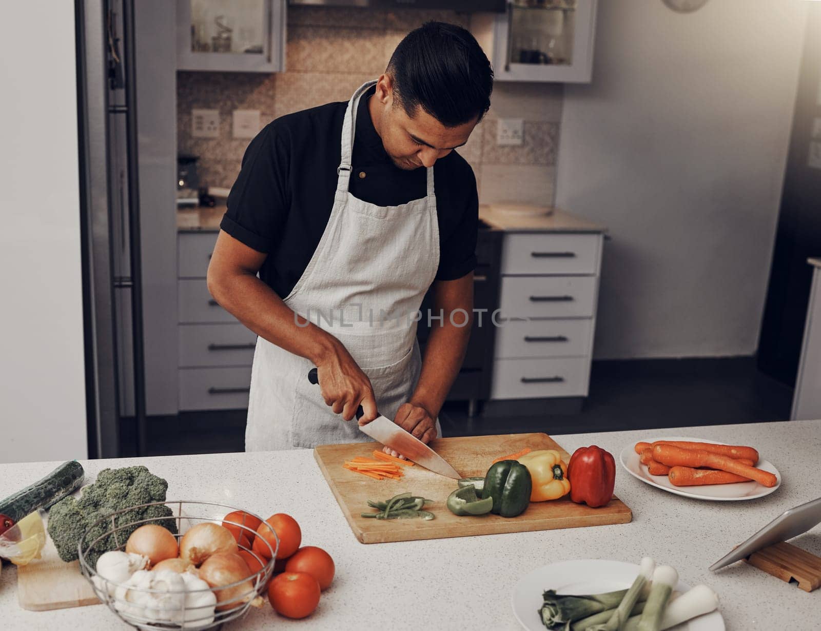Cooking, food and vegetables with a man cutting ingredients in the kitchen on a wooden chopping board. Salad, health and diet with a male chef preparing a meal while standing alone in his home.