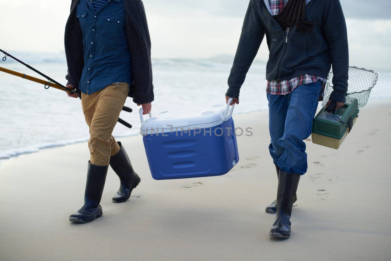 Carrying their tackle. Two fisherman carrying a cooler and a tackle box on the beach in the early morning