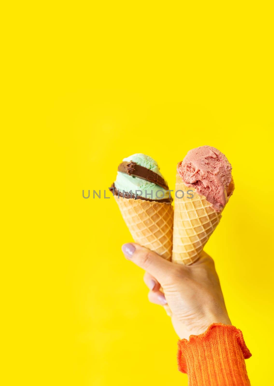 A cone of refreshing ice cream in a waffle cup against a yellow wall. The concept of vacation, vacation at sea. A woman holds ice cream in her hands. Vertical photo