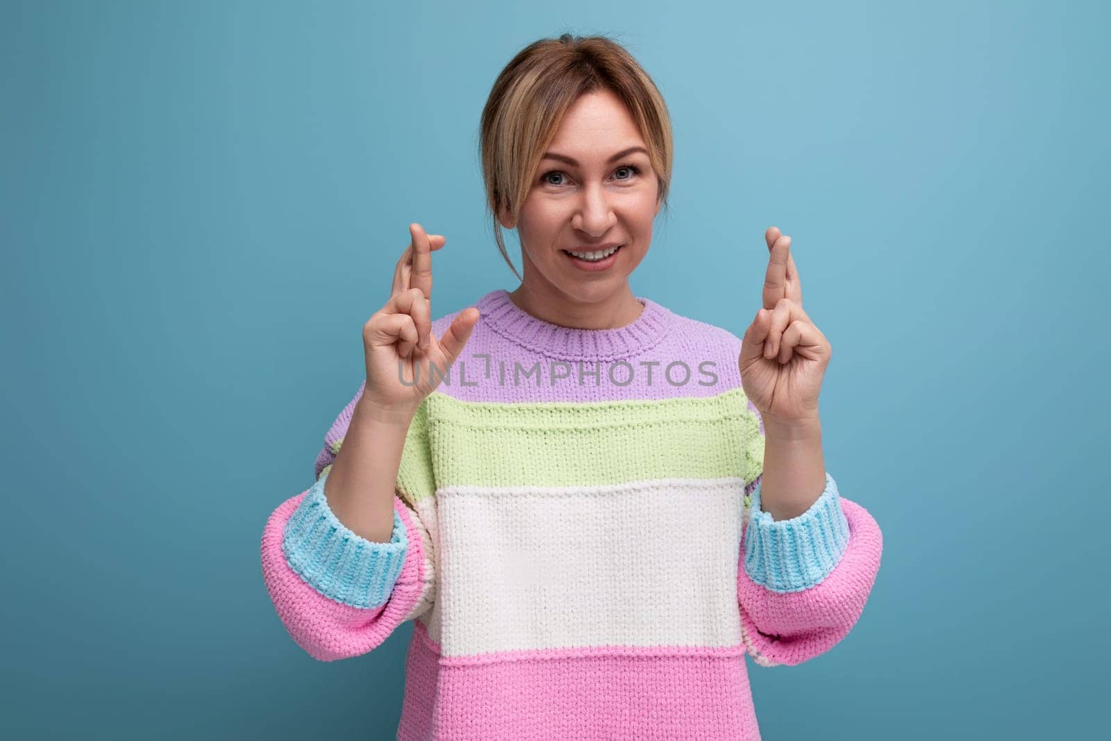 cute blond woman in casual look crossed her arms and hopes on blue background.
