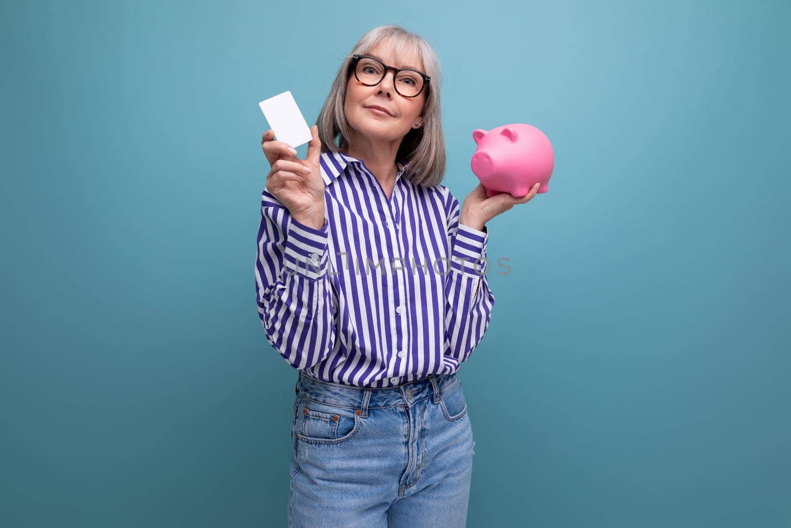 social protection. 60s middle aged woman with gray hair holding a piggy bank against a bright studio background by TRMK