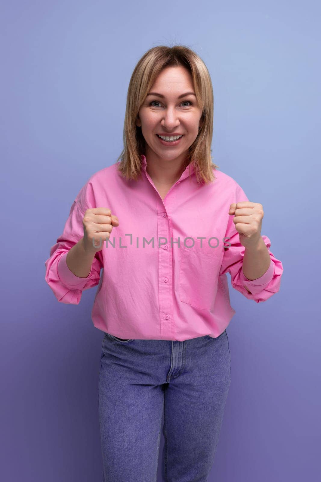 young well-groomed blond caucasian woman with flowing straight hair is dressed in a pink blouse and jeans.
