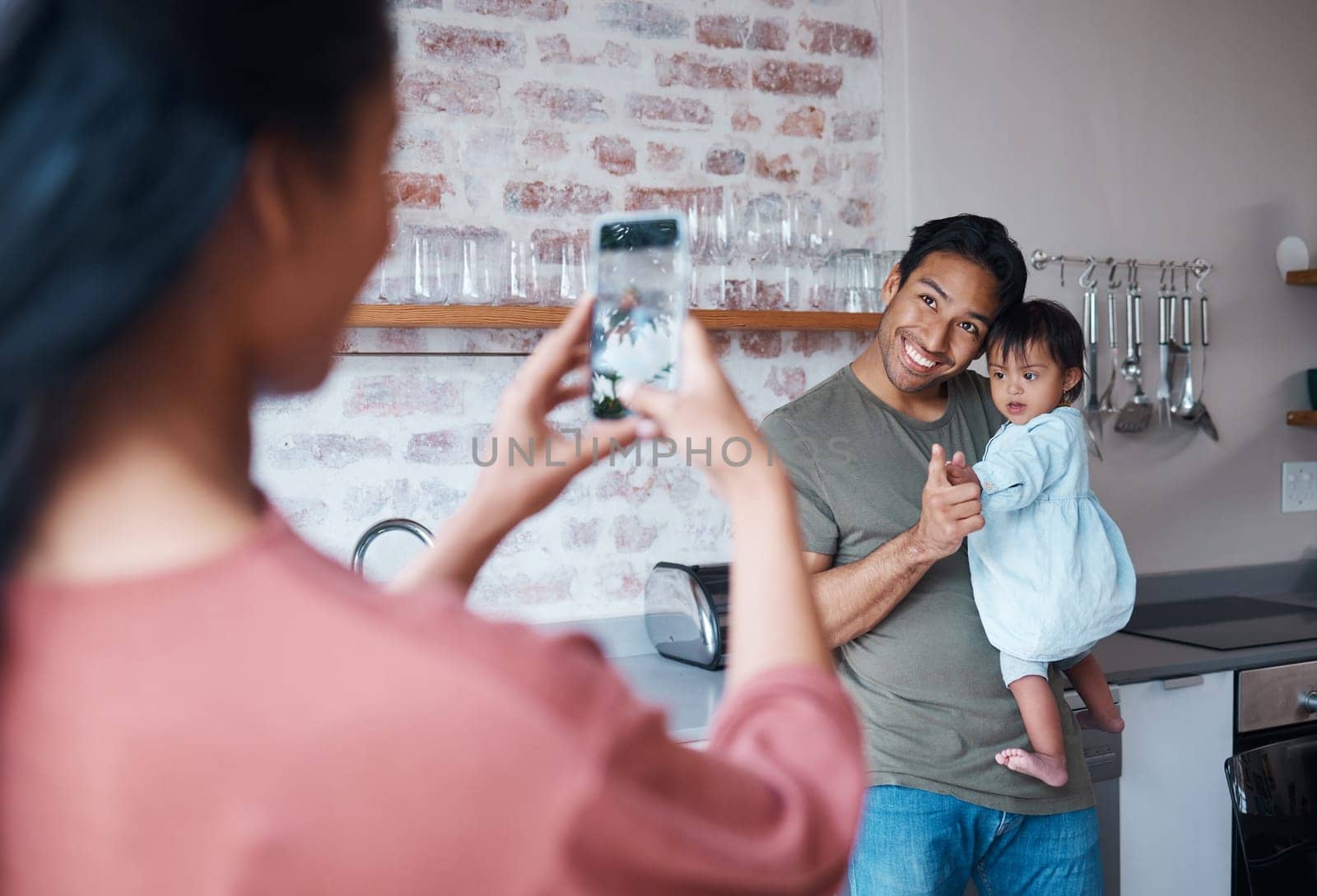 Family, care and mother with phone for photo of father and baby with down syndrome in the living room of their house. Mom taking a picture of a happy dad and child with special needs on a smartphone.