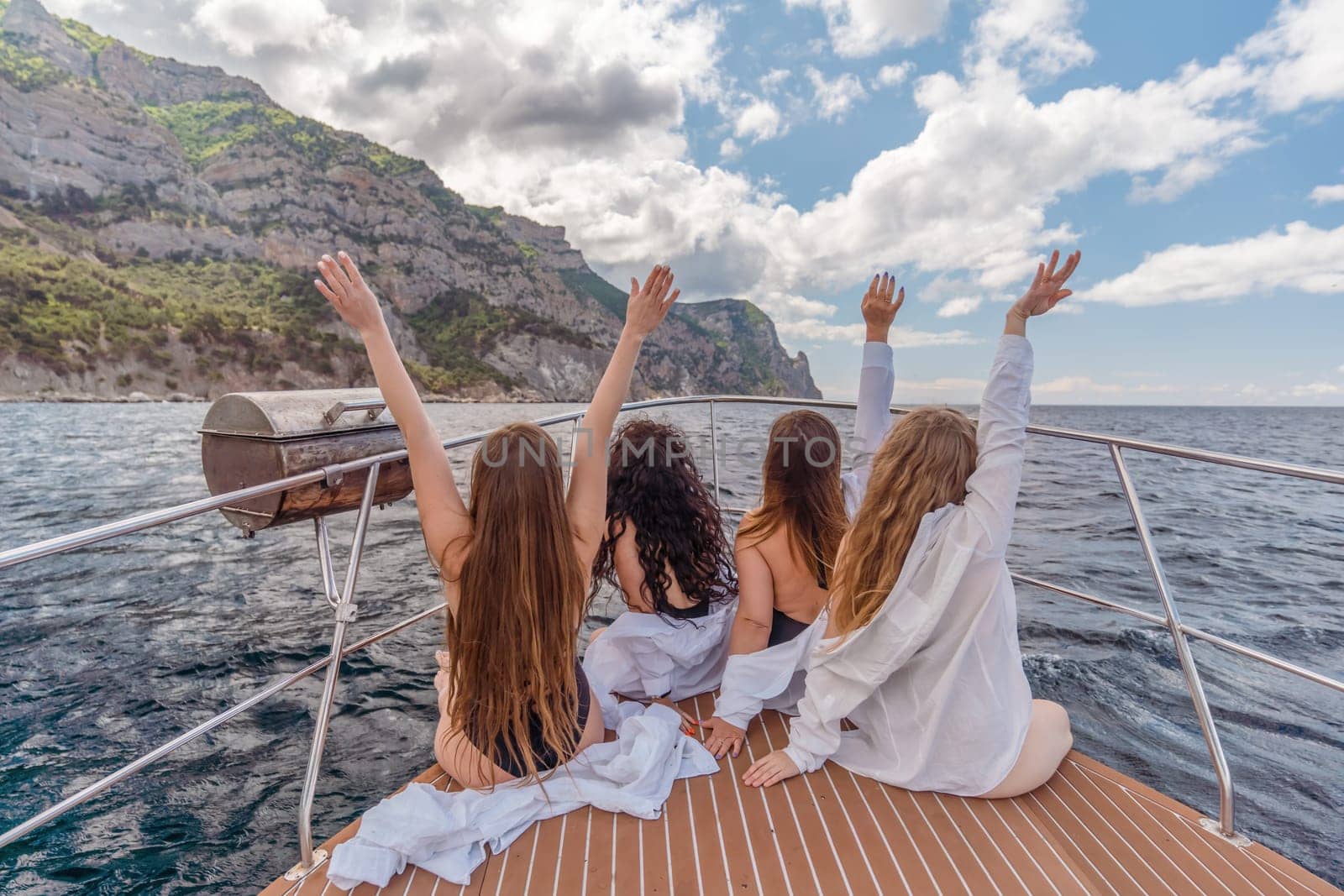 Womans on a yacht. Happy models in a swimsuit posing on a yacht against a blue sky with clouds and mountains.