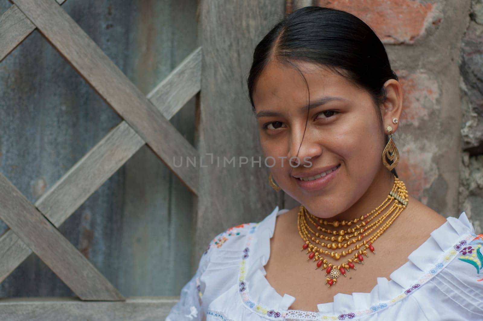 native latin america girl looking at camera and smiling wearing traditional dress of her culture and gold earrings and necklaces by Raulmartin