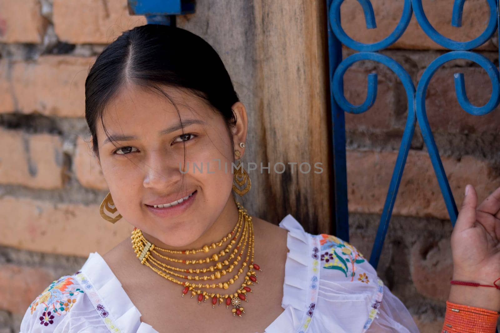 closeup of indigenous teenager from otavalo smiling at the camera tied to a blue fence by Raulmartin