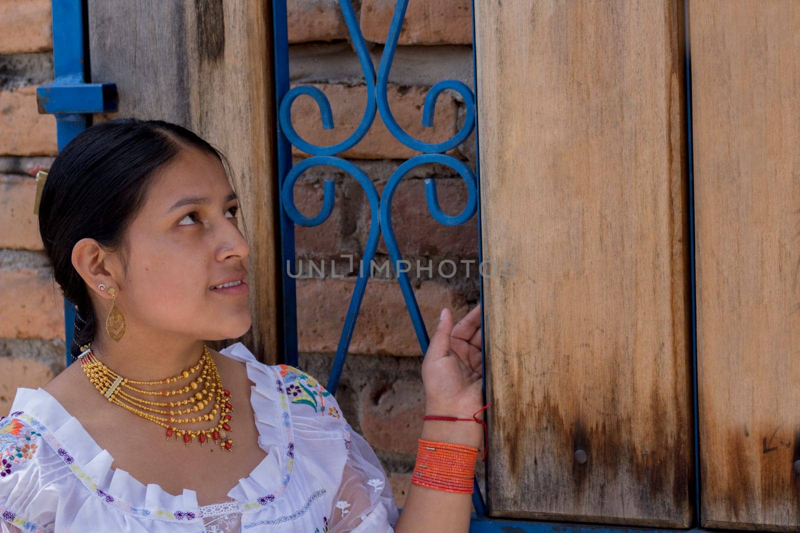 closeup with copy space of a beautiful indigenous girl in dress from the native culture of ecuador next to a wooden door and blue fence. High quality photo