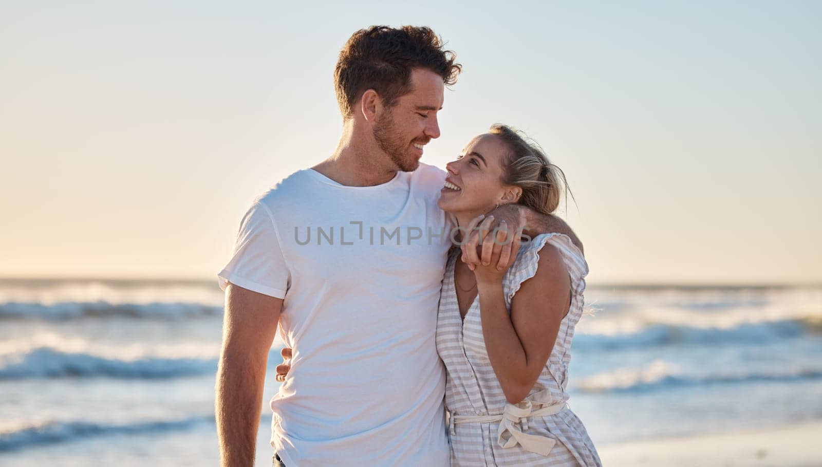 Sunset beach, love and summer with a couple hug on the sand by the sea or ocean while on holiday together. Happy, smile and romance with man and woman bonding while on travel vacation or break at sea by YuriArcurs