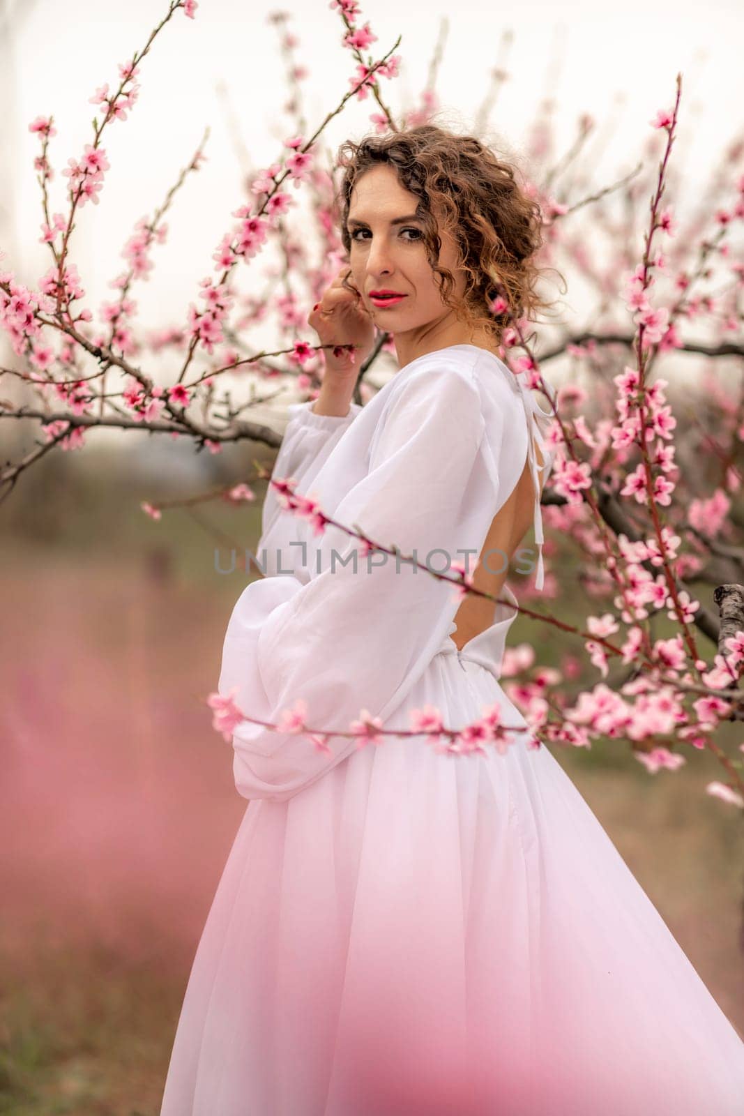 Woman peach blossom. Happy curly woman in white dress walking in the garden of blossoming peach trees in spring by Matiunina