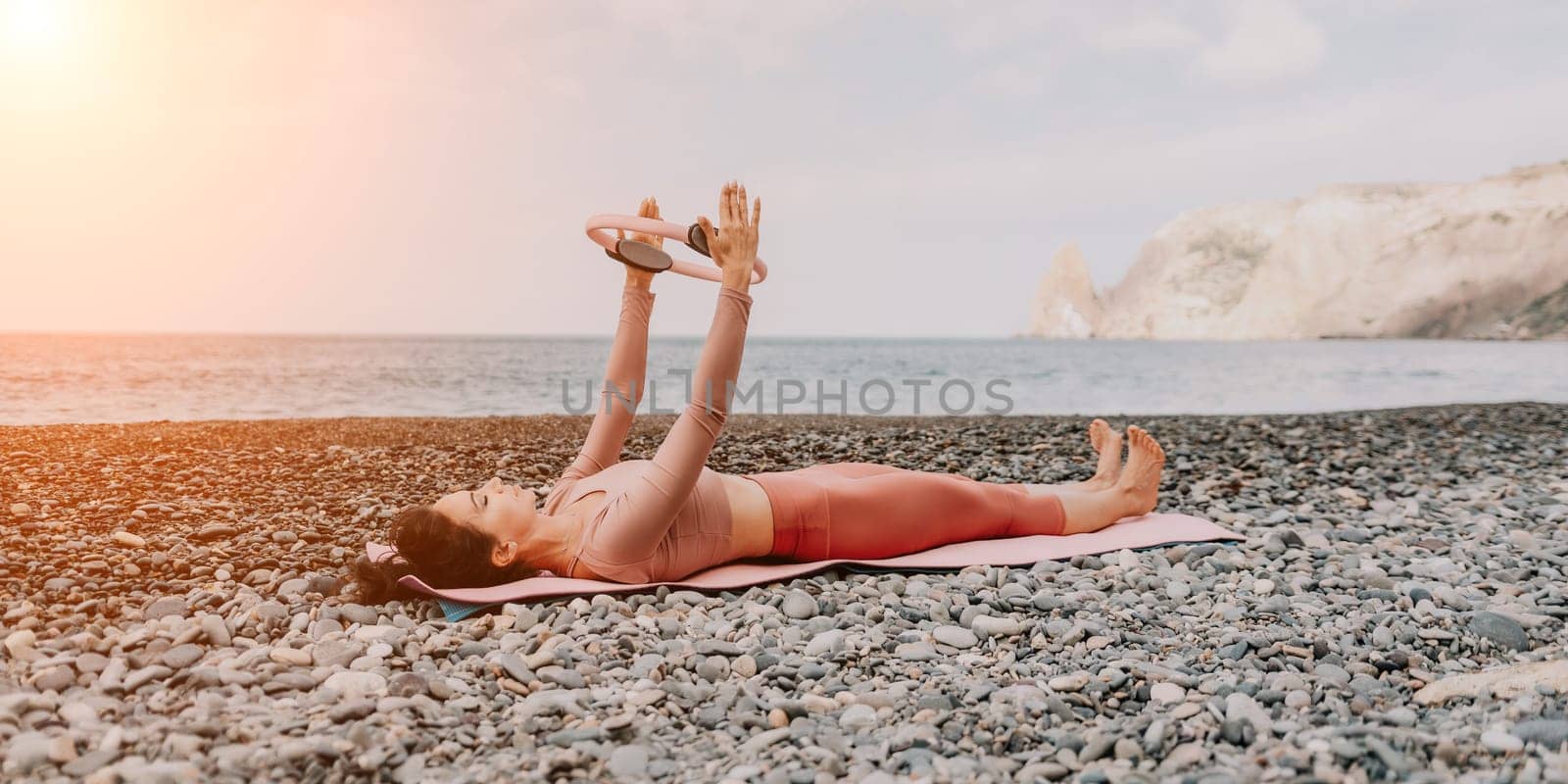 Woman sea pilates. Sporty happy middle aged woman practicing fitness on beach near sea, smiling active female training with ring on yoga mat outside, enjoying healthy lifestyle, harmony and meditation by panophotograph