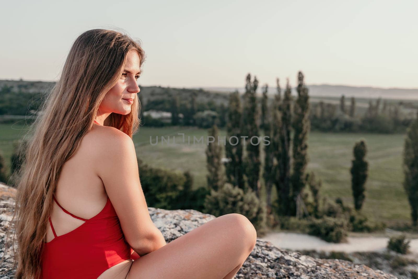 Well looking middle aged woman with long hair, fitness instructor in leggings and tops doing stretching and pilates on the rock near forest. Female fitness yoga routine concept. Healthy lifestyle by panophotograph