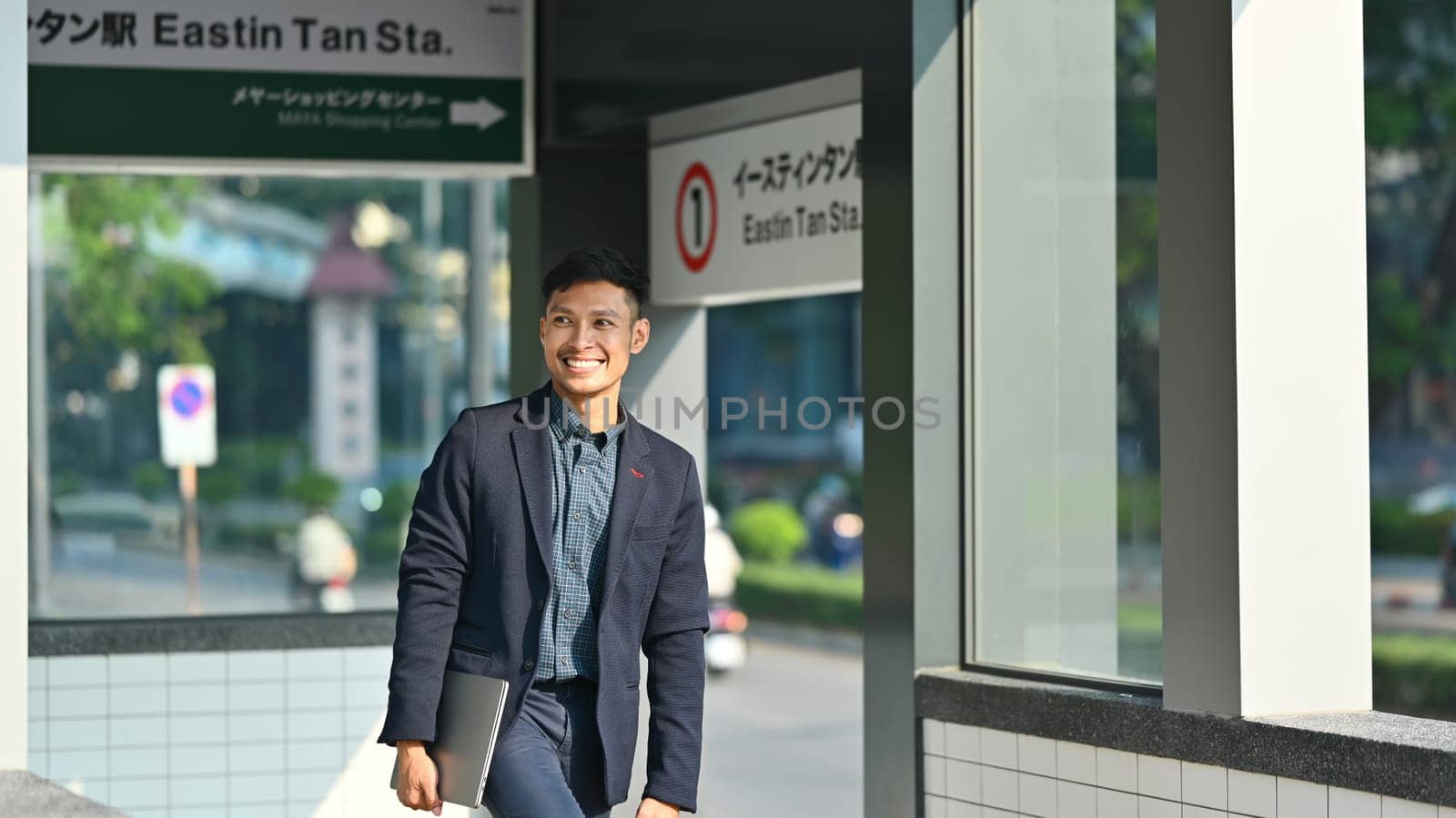 Smiling millennial man in business suit walking in subway station during his morning commute.
