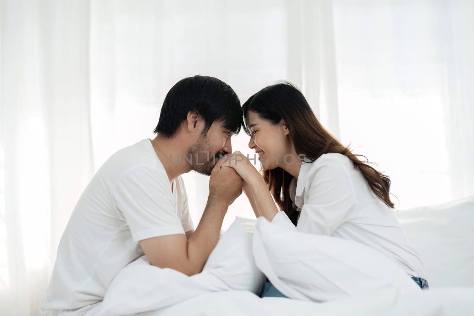 Young couple sitting in bed with pillows in modern bedroom.