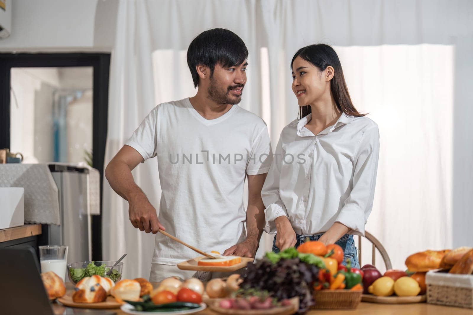 Happy smiling couple cooking together and healthy eating concept - couple cooking food at home kitchen.
