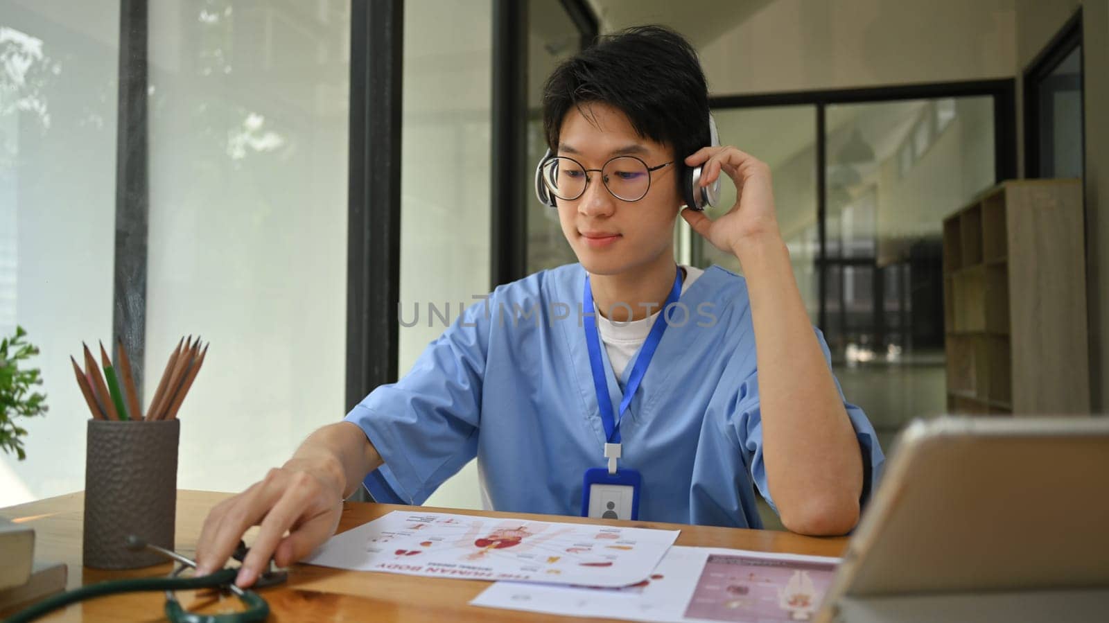 Concentrated male medical students wearing headphone and reading book in library. Education and Technology concept.