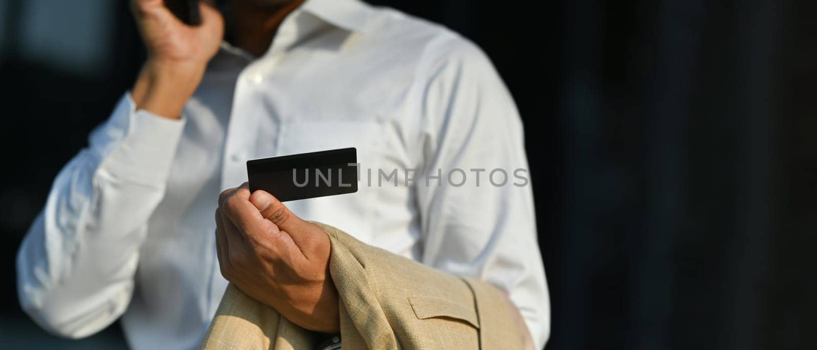 Businessman holding credit card and talking on smartphone with customer service, having problem with credit card or payment.