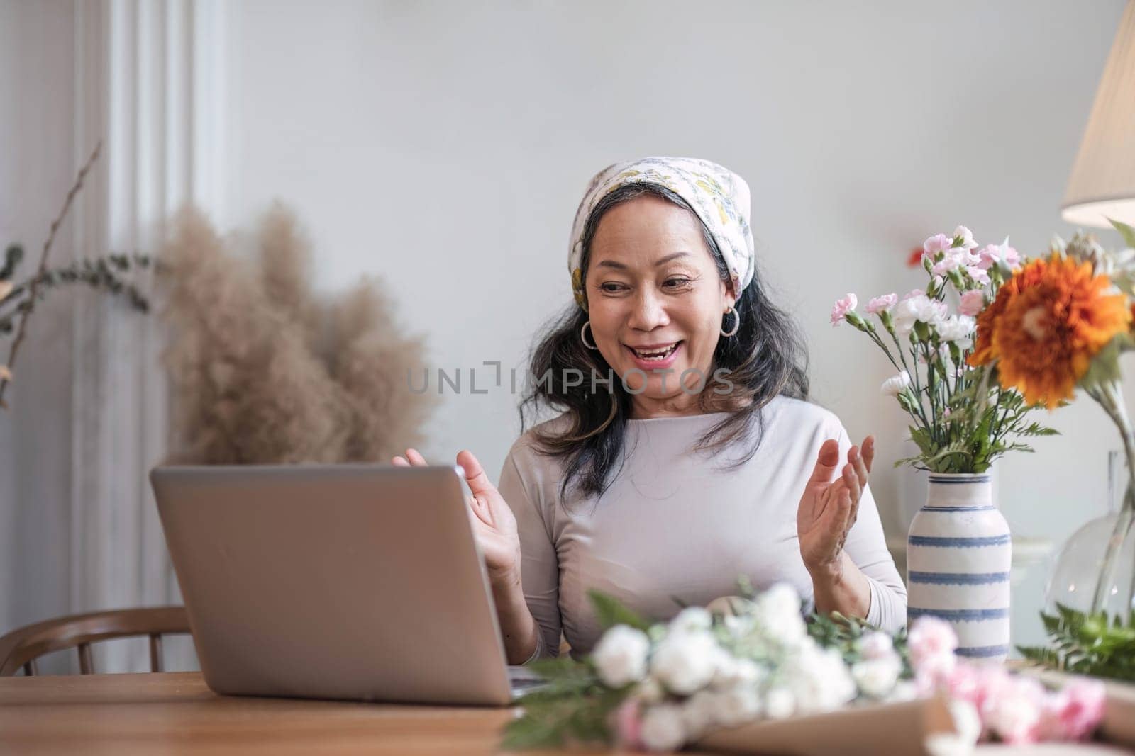 Happy and attractive mature Asian woman enjoying with her online flower arrangement workshop at home. by wichayada