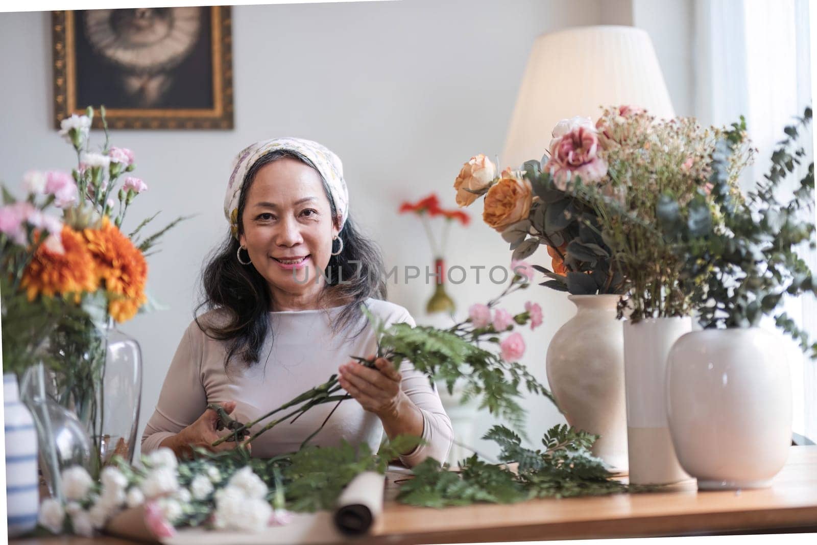Happy and attractive mature Asian woman enjoying with her online flower arrangement workshop at home. by wichayada