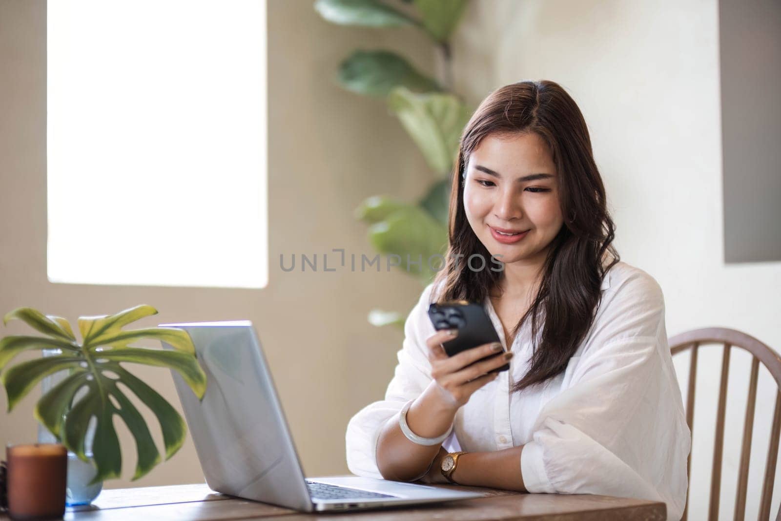 Attractive and happy young Asian girl reading a book and use laptop at a table in her minimal living room. Hobby and leisure concepts by wichayada