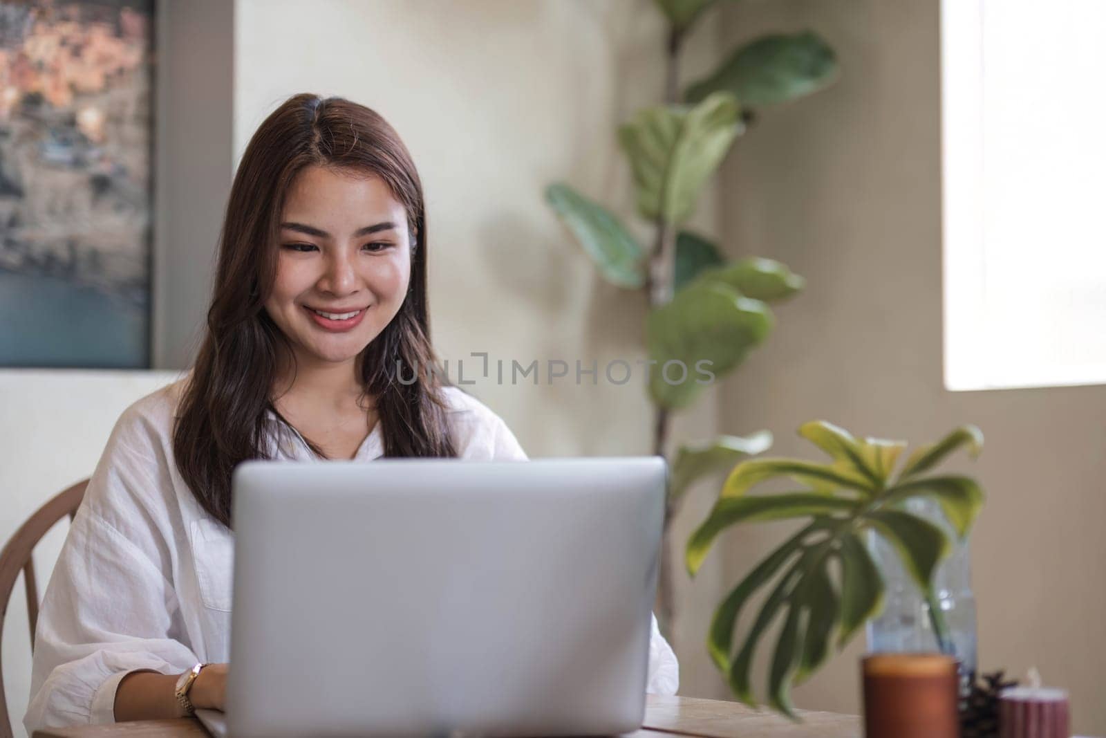 Attractive and happy young Asian girl reading a book and use laptop at a table in her minimal living room. Hobby and leisure concepts by wichayada