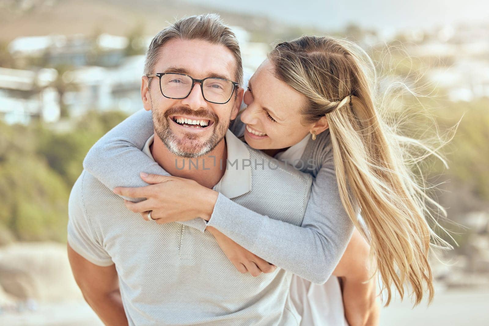 Beach, piggy back and couple with love, relationship and happiness with romantic holiday, weekend trip and marriage. Portrait, mature man and woman with a smile, hug and seaside vacation with romance by YuriArcurs