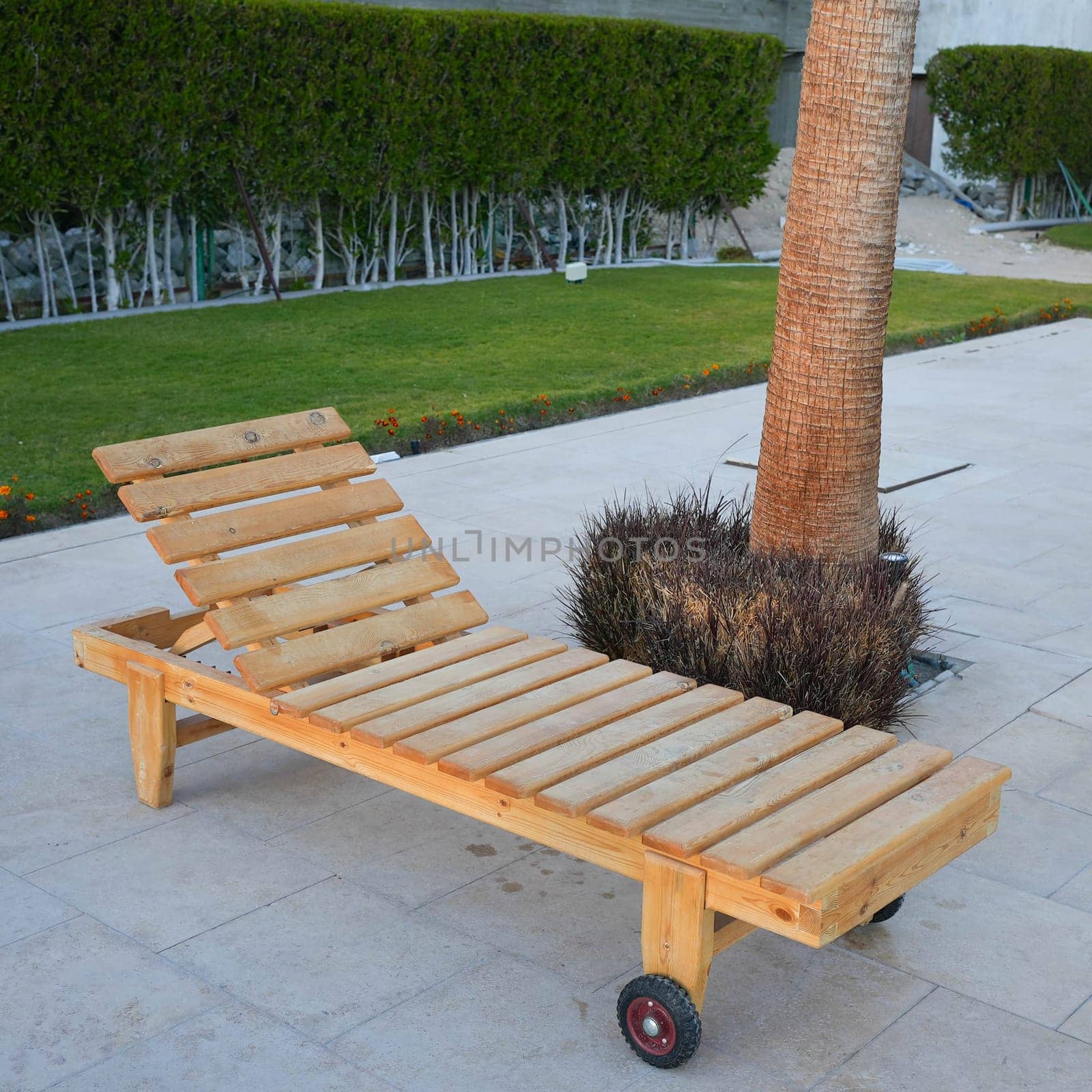 Empty wooden sunbed deck chair on tiles in a garden with grass. High quality photo