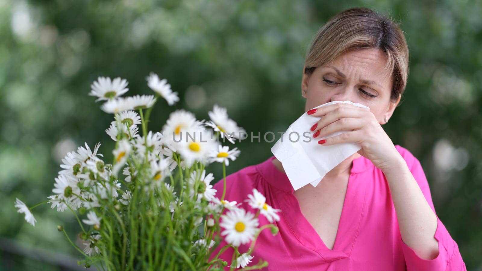 Young woman with hay fever blowing her nose in napkin near chamomile flowers. Allergic diseases concept