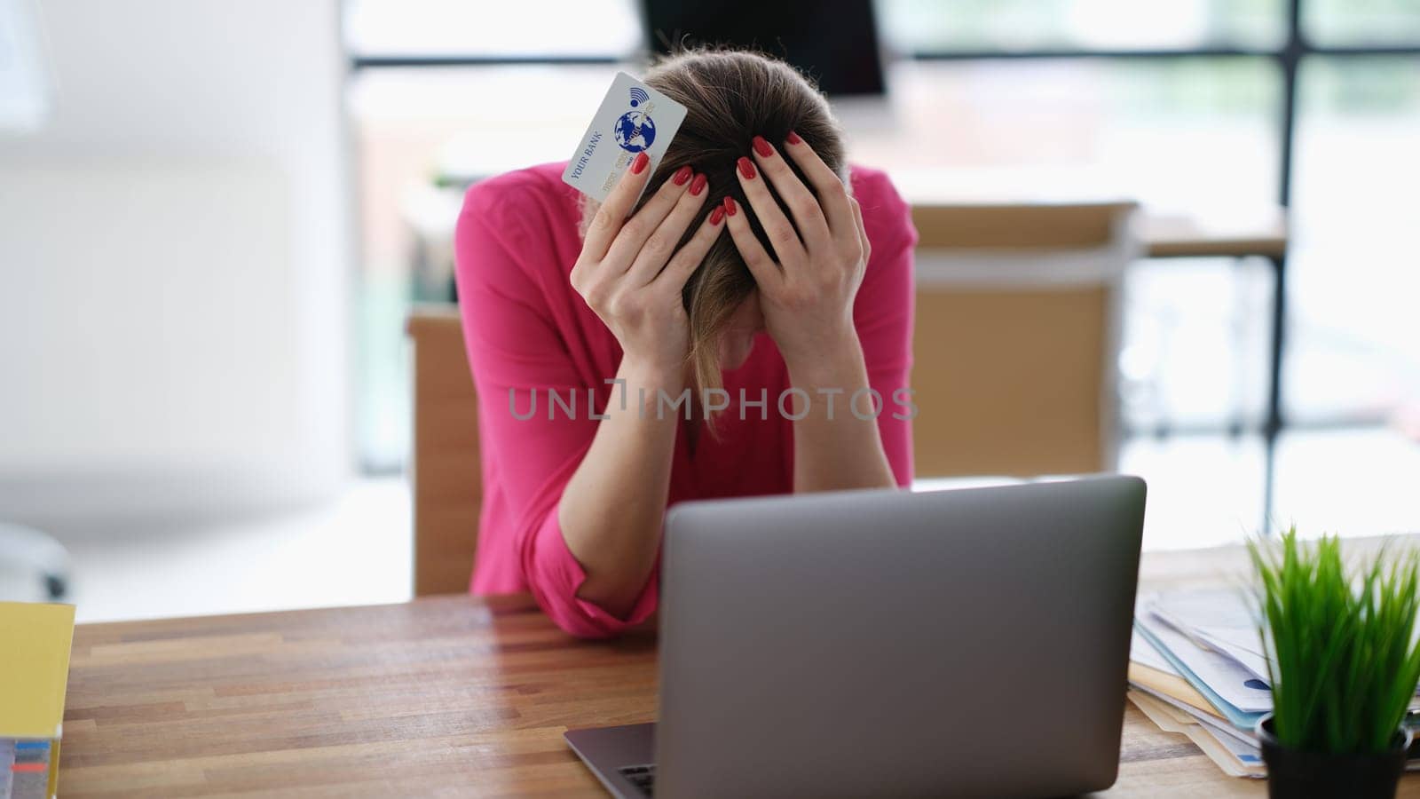 Upset woman sitting at laptop with credit plastic card and holding his head. Internet scam concept
