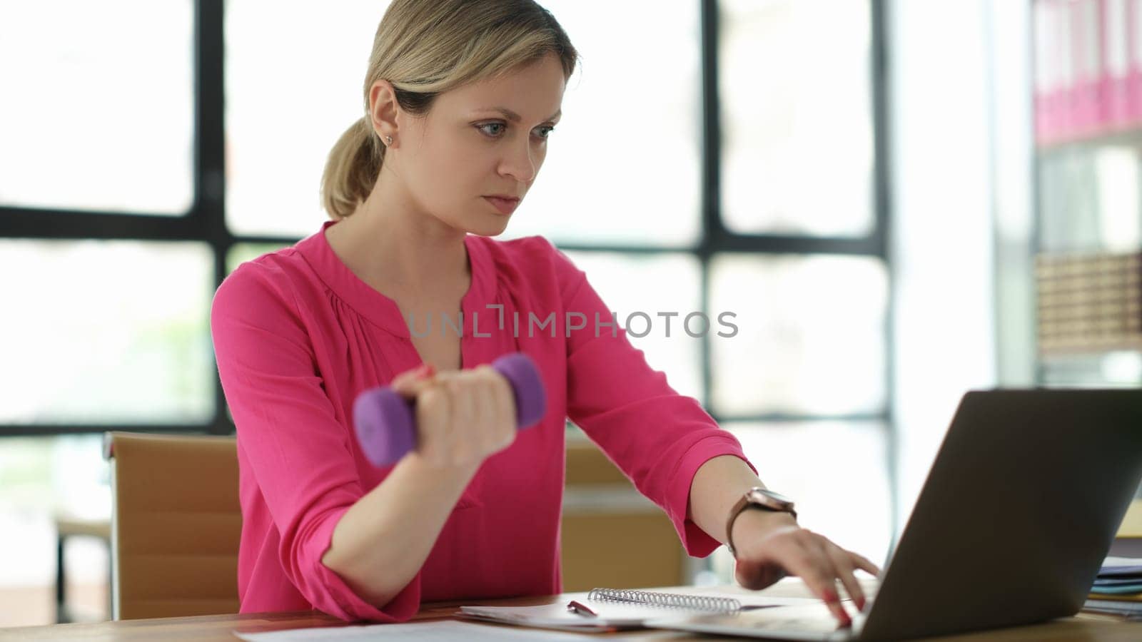 Businesswoman lifting dumbbell and working on laptop in office. Feminism and success of women in business concept