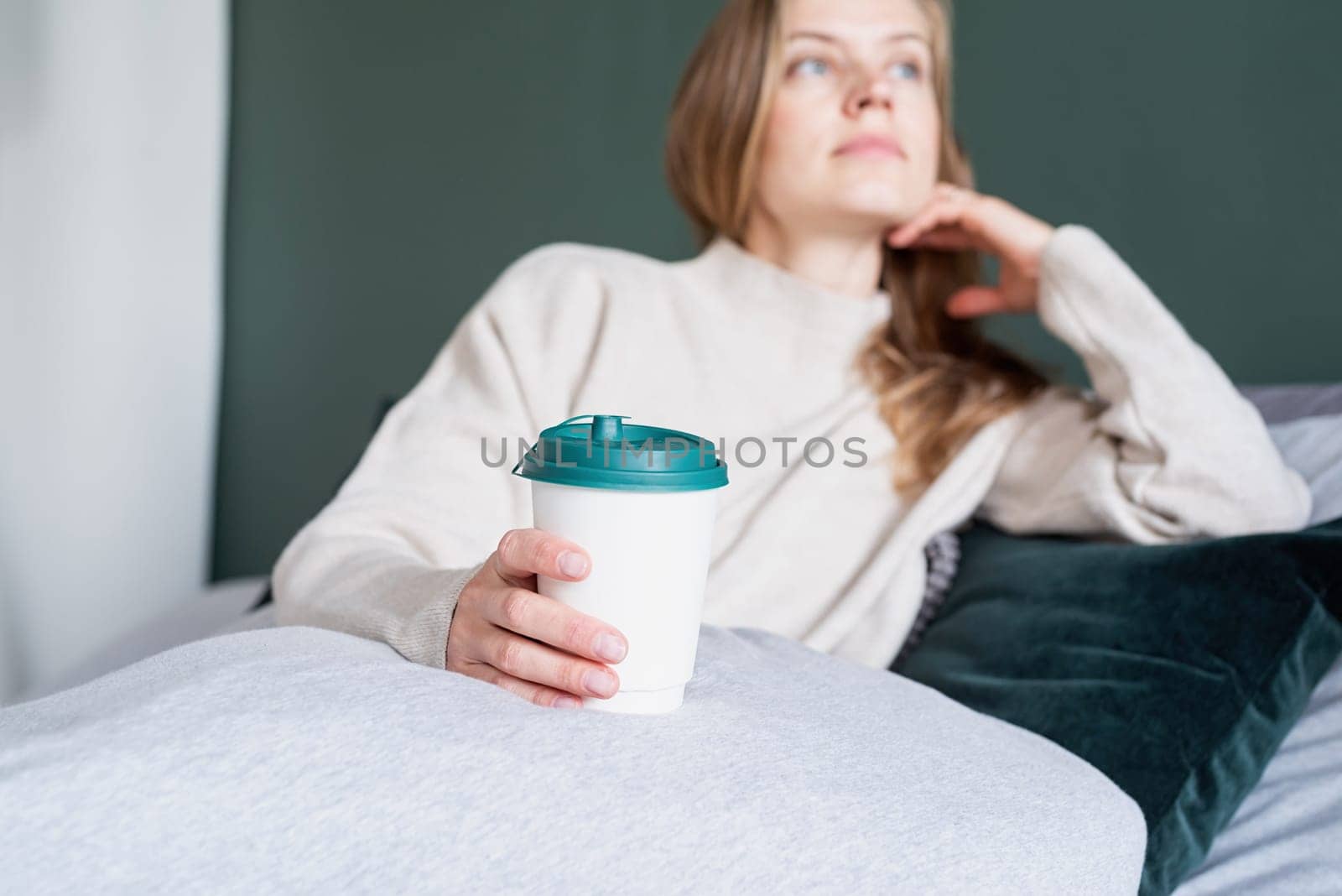 caucasian woman waking up in her bed in the morning. young millennial woman sitting on the bed in the morning drinking coffee from paper cup, mockup design