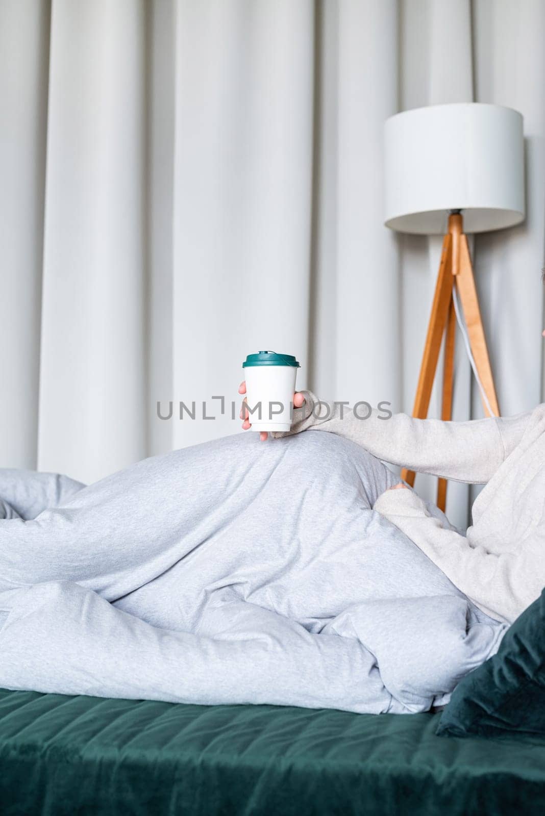 caucasian woman waking up in her bed in the morning. young millennial woman sitting on the bed in the morning drinking coffee from paper cup, mockup design